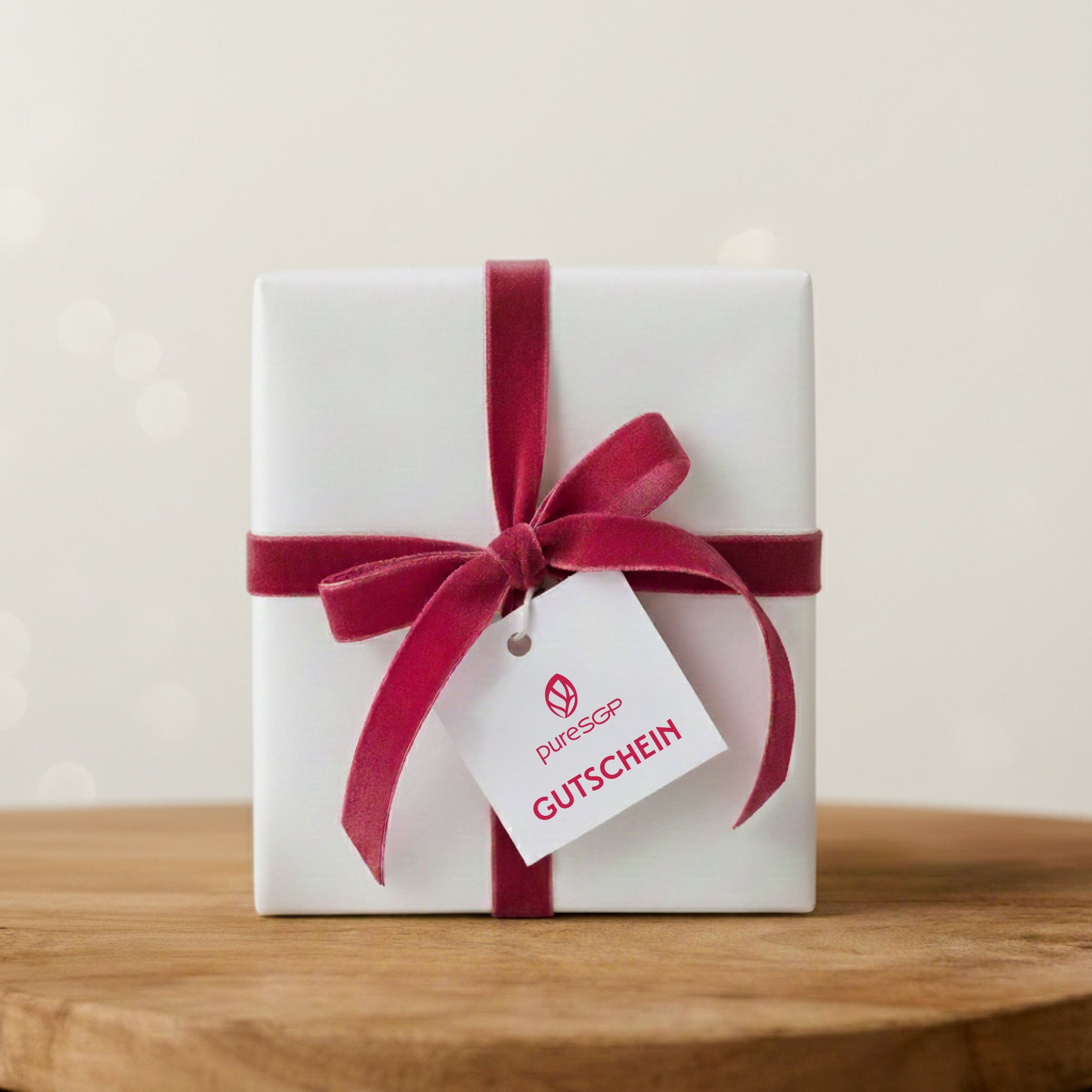 Weiß verpacktes Geschenk mit roter Schleife steht auf einer Holzfläche. An der Schleife hängt ein Etikett mit der Aufschrift ‚pureSGP Gutschein‘.